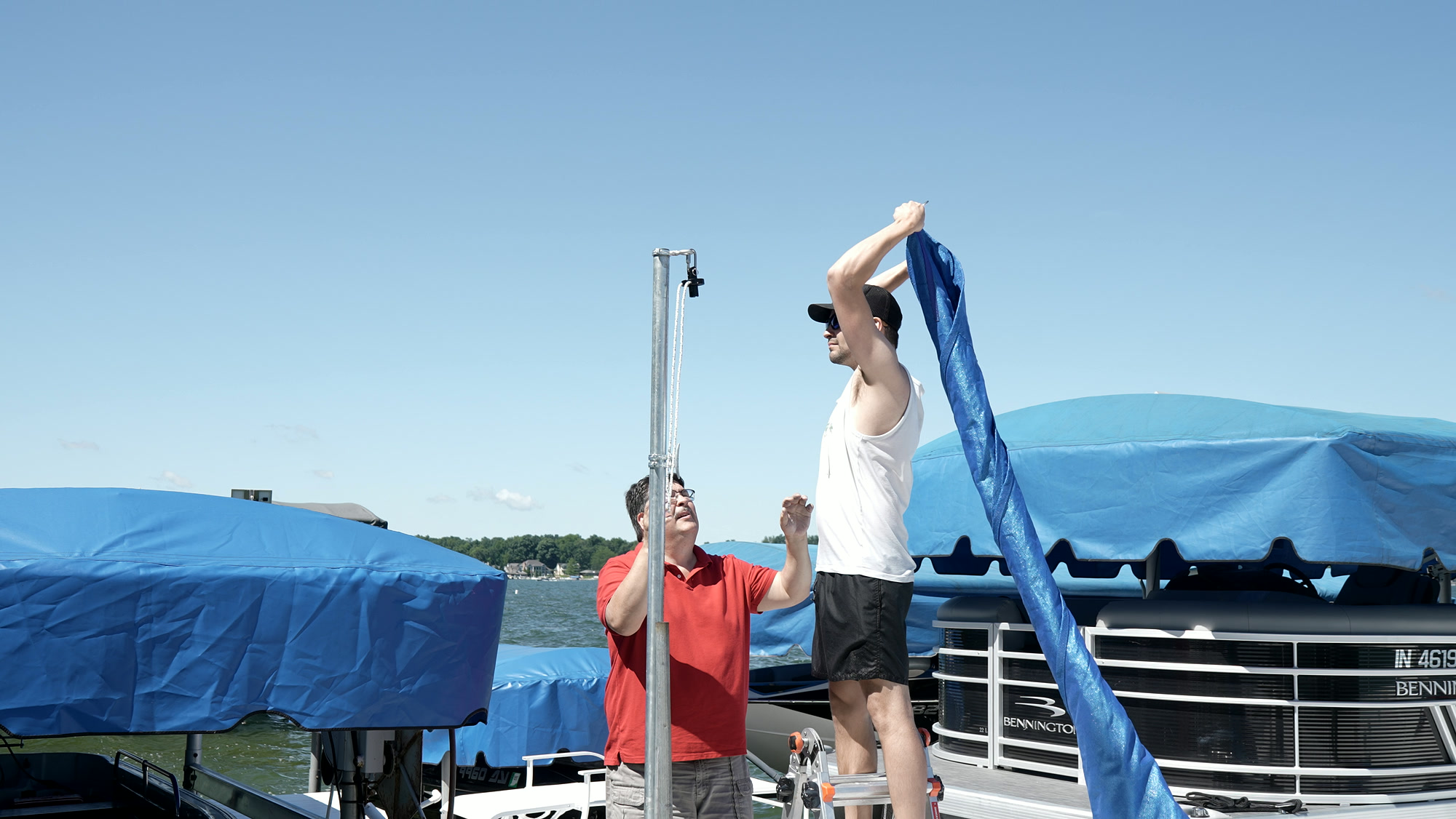 Two DockShade installers raising a blue custom shade beside its galvanized post